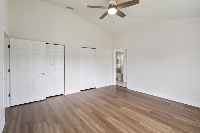 unfurnished bedroom with ceiling fan, wood-type flooring, high vaulted ceiling, and ensuite bath