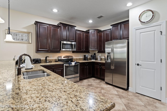 kitchen with appliances with stainless steel finishes, dark brown cabinets, a textured ceiling, sink, and decorative light fixtures