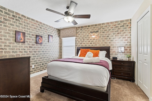 carpeted bedroom with ceiling fan, a closet, brick wall, and a textured ceiling