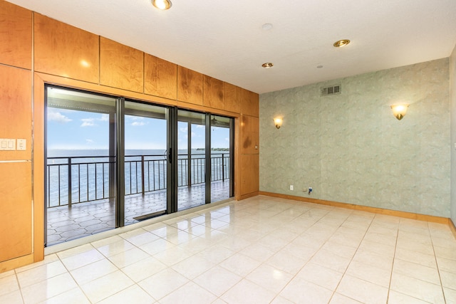 empty room with wooden walls, a water view, a healthy amount of sunlight, and a textured ceiling