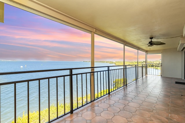 balcony at dusk featuring ceiling fan and a water view