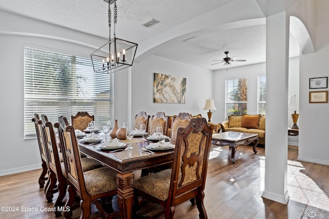 dining area with ceiling fan with notable chandelier, a textured ceiling, and hardwood / wood-style flooring