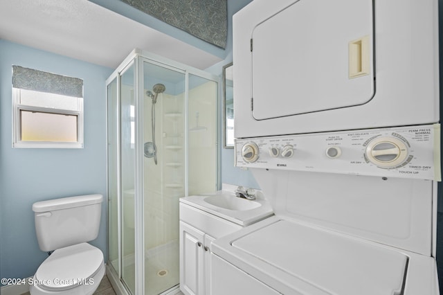 bathroom with vanity, stacked washing maching and dryer, a shower with shower door, and toilet