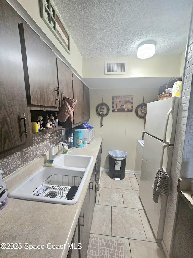 kitchen with dark brown cabinetry, sink, white refrigerator, a textured ceiling, and light tile patterned floors