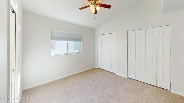 unfurnished bedroom with ceiling fan, vaulted ceiling, light carpet, and multiple closets