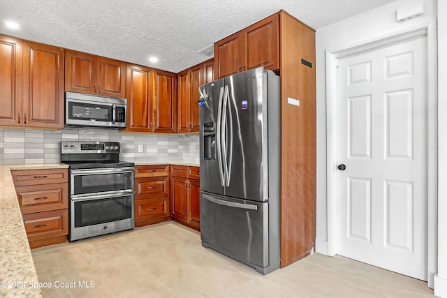 kitchen with a textured ceiling, light stone countertops, backsplash, and appliances with stainless steel finishes