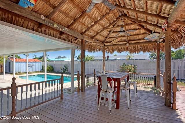 wooden terrace featuring a gazebo, ceiling fan, a fenced in pool, and a storage shed