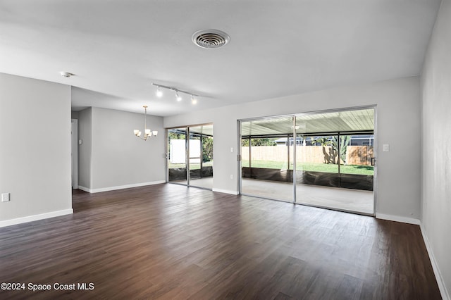 spare room featuring dark hardwood / wood-style floors, track lighting, and an inviting chandelier