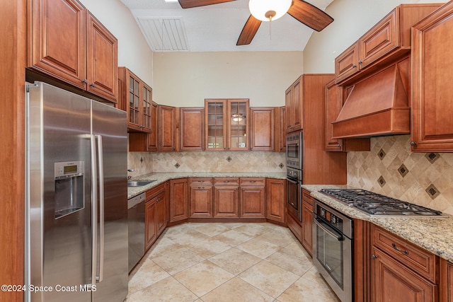 kitchen with decorative backsplash, appliances with stainless steel finishes, light stone counters, custom exhaust hood, and ceiling fan