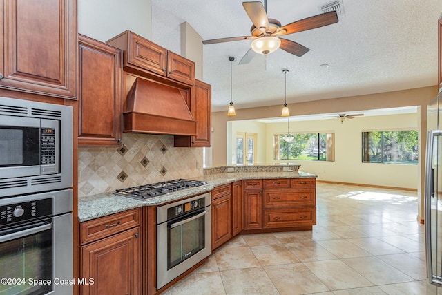 kitchen with hanging light fixtures, stainless steel appliances, light stone counters, decorative backsplash, and custom range hood