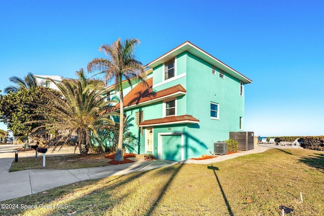 exterior space with an attached garage, cooling unit, driveway, a lawn, and stucco siding