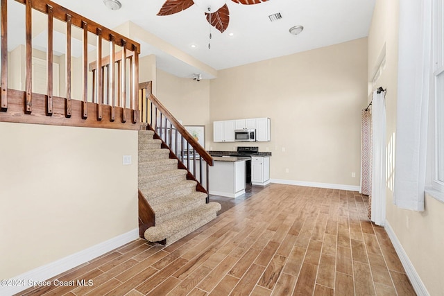 foyer entrance featuring a ceiling fan, baseboards, visible vents, light wood-style floors, and stairway