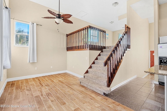 staircase featuring a ceiling fan, baseboards, and wood finished floors