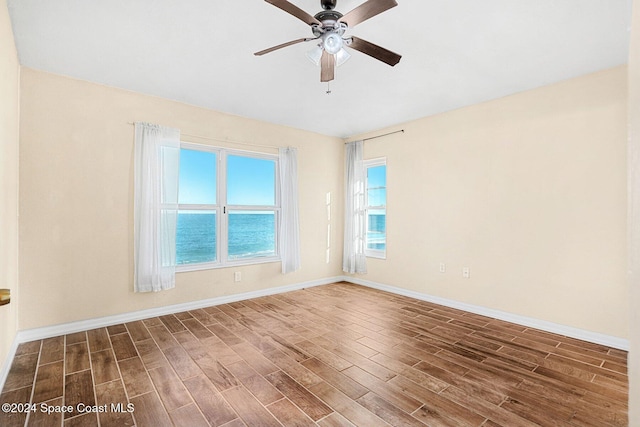 empty room with dark wood-style floors, a water view, baseboards, and a ceiling fan