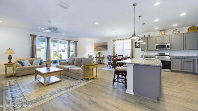 living room with ceiling fan, sink, and light wood-type flooring