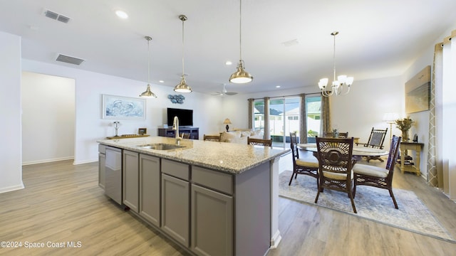 kitchen with a center island with sink, sink, decorative light fixtures, gray cabinets, and light stone countertops