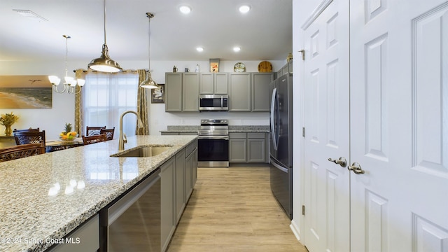 kitchen featuring appliances with stainless steel finishes, sink, gray cabinetry, decorative light fixtures, and light stone countertops