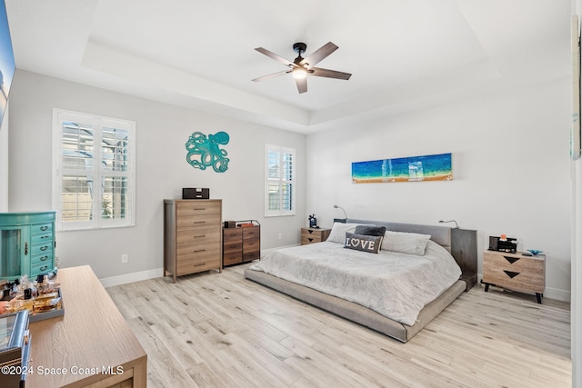 bedroom with a tray ceiling, multiple windows, ceiling fan, and light hardwood / wood-style flooring