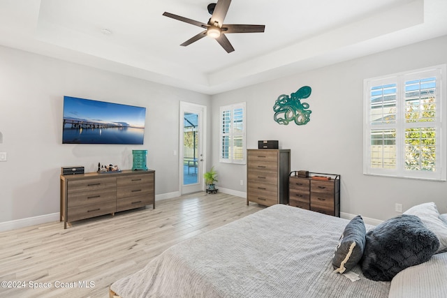 bedroom featuring a raised ceiling, access to exterior, light hardwood / wood-style floors, and multiple windows