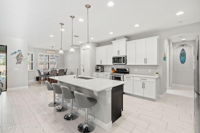 kitchen featuring a center island with sink, white cabinets, decorative light fixtures, and appliances with stainless steel finishes