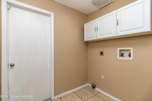 laundry room with electric dryer hookup, cabinets, hookup for a washing machine, light tile patterned floors, and a textured ceiling