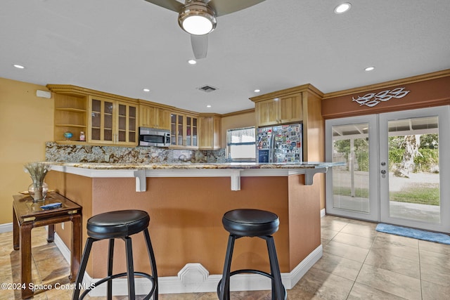 kitchen featuring kitchen peninsula, appliances with stainless steel finishes, backsplash, french doors, and a kitchen breakfast bar