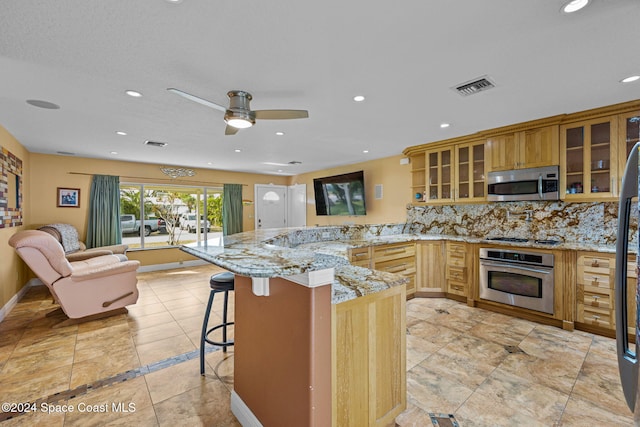 kitchen with kitchen peninsula, light stone counters, a breakfast bar, and appliances with stainless steel finishes