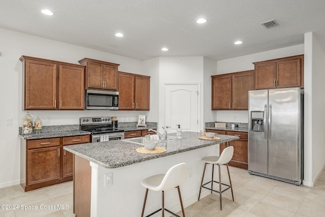 kitchen with appliances with stainless steel finishes, a breakfast bar, a textured ceiling, sink, and a center island with sink