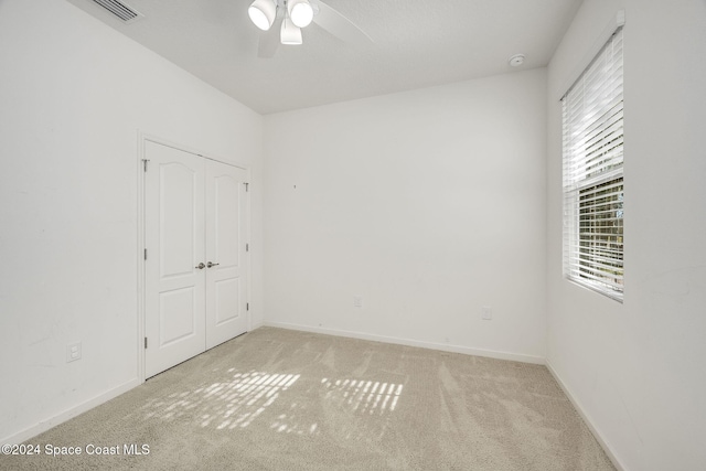 unfurnished bedroom featuring a closet, light colored carpet, and ceiling fan