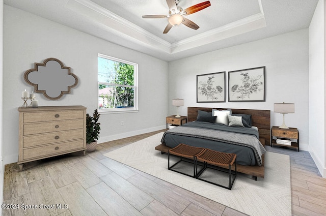 bedroom featuring ceiling fan, crown molding, a tray ceiling, and light hardwood / wood-style flooring