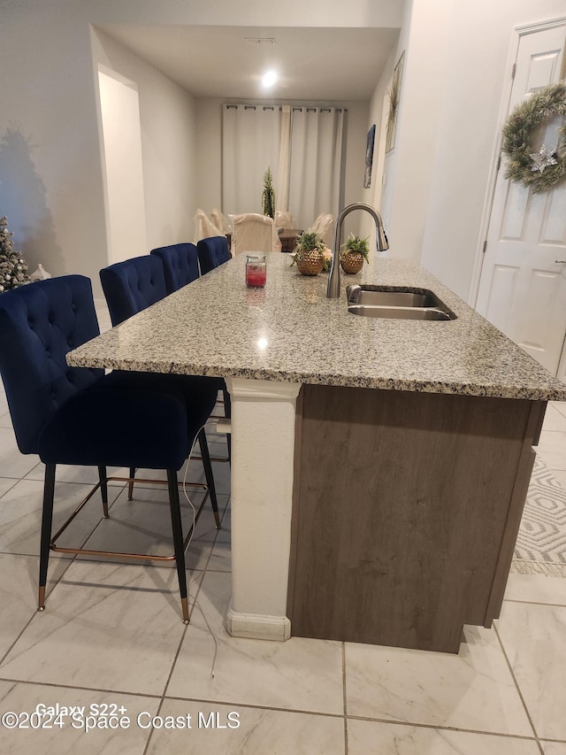 kitchen featuring a kitchen island with sink, a breakfast bar, light stone countertops, and sink