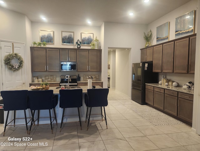 kitchen with a center island with sink, sink, a breakfast bar area, light stone countertops, and stainless steel appliances