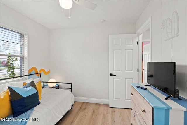 bedroom featuring ceiling fan, light hardwood / wood-style floors, wooden walls, and multiple windows