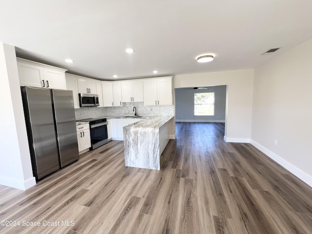 kitchen with kitchen peninsula, appliances with stainless steel finishes, sink, hardwood / wood-style flooring, and white cabinets