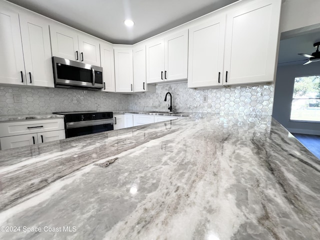 kitchen featuring white cabinets, black range with electric cooktop, light stone counters, and sink