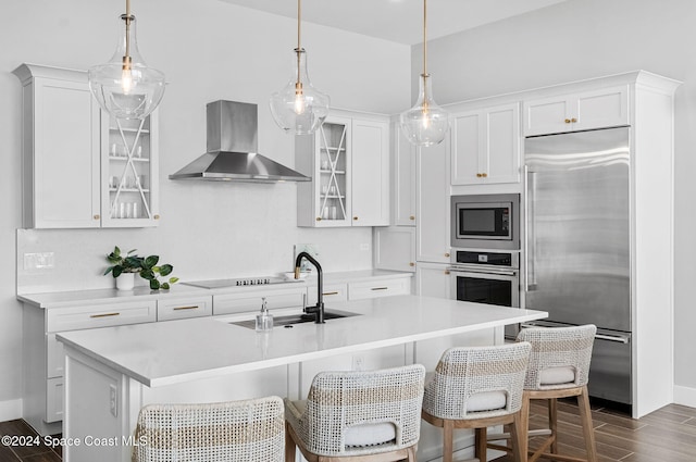 kitchen featuring built in appliances, white cabinetry, and wall chimney exhaust hood