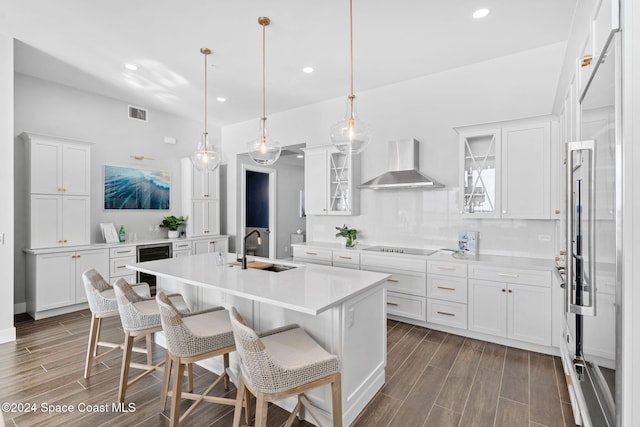 kitchen with a breakfast bar, white cabinets, sink, wall chimney exhaust hood, and an island with sink