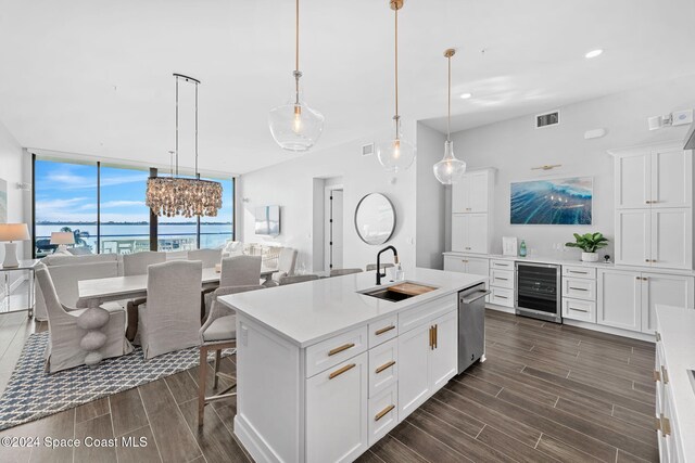 kitchen with sink, hanging light fixtures, beverage cooler, a center island with sink, and a water view