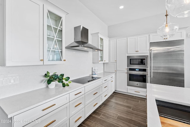 kitchen with dark wood-type flooring, wall chimney range hood, built in appliances, pendant lighting, and white cabinets