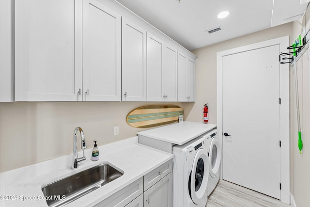 washroom with cabinets, washing machine and dryer, light hardwood / wood-style flooring, and sink