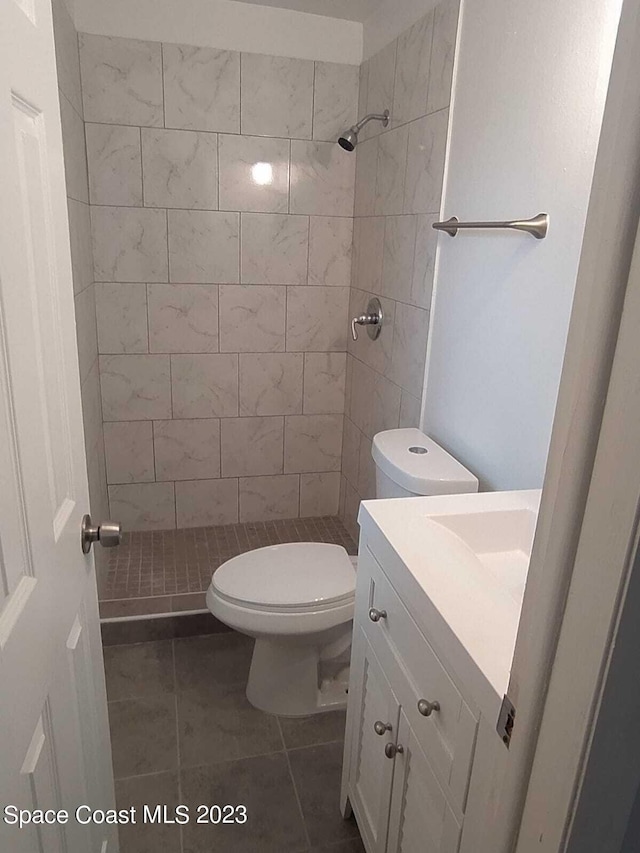 bathroom featuring tile patterned floors, toilet, a tile shower, and vanity