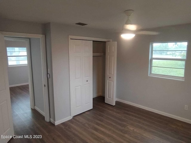 unfurnished bedroom featuring a closet, multiple windows, dark wood-type flooring, and ceiling fan