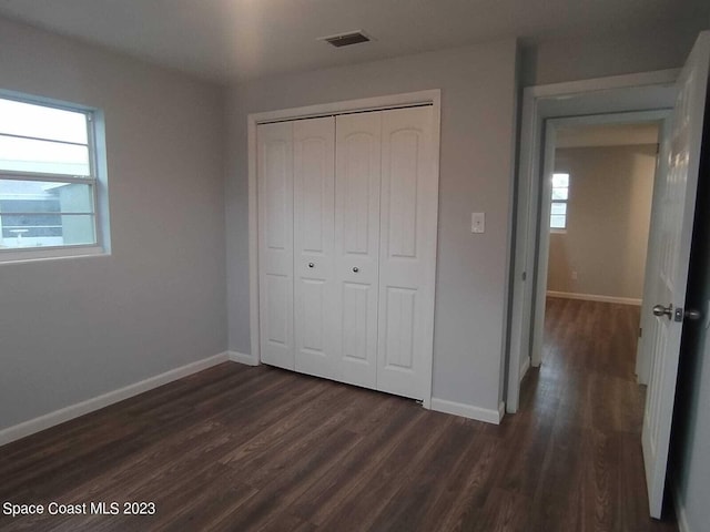 unfurnished bedroom featuring multiple windows, a closet, and dark wood-type flooring