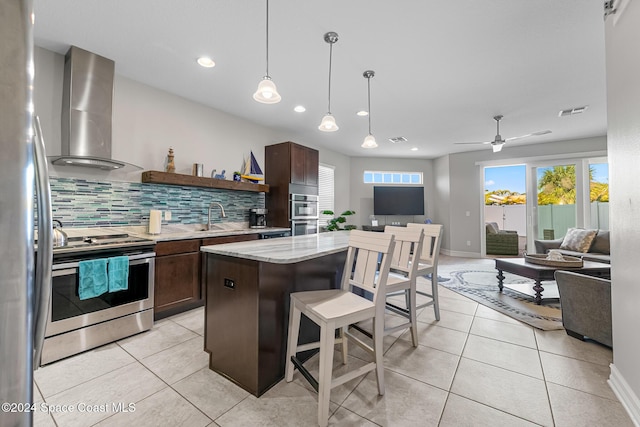 kitchen with tasteful backsplash, wall chimney exhaust hood, stainless steel appliances, decorative light fixtures, and a center island