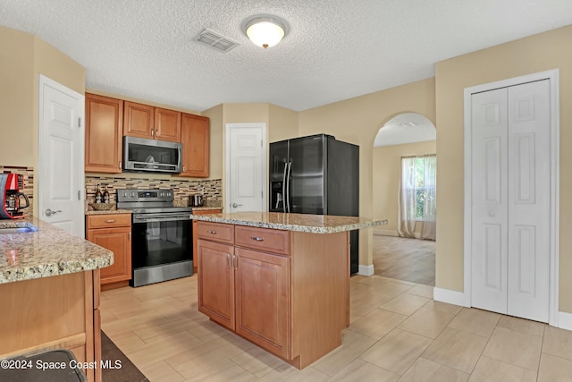 kitchen featuring light stone countertops, a textured ceiling, tasteful backsplash, a kitchen island, and stainless steel appliances