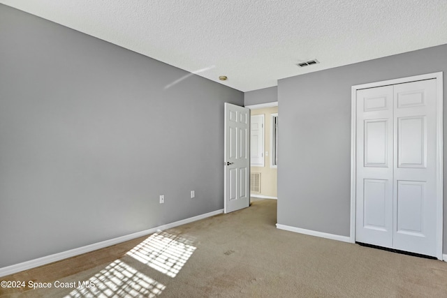 unfurnished bedroom with a textured ceiling, light carpet, and a closet