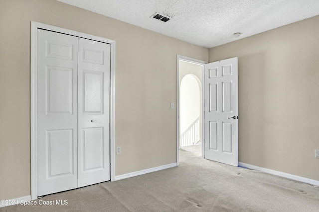 unfurnished bedroom featuring a textured ceiling, light colored carpet, and a closet