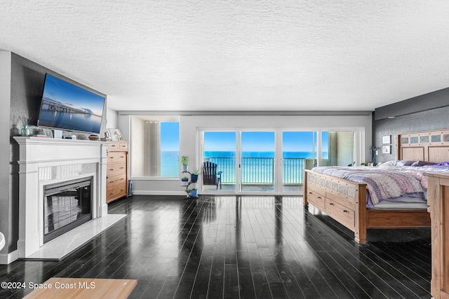 bedroom with access to exterior, a textured ceiling, a water view, and dark hardwood / wood-style floors