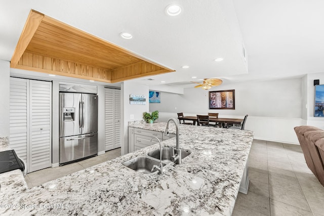 kitchen with ceiling fan, sink, stainless steel fridge with ice dispenser, light stone counters, and range