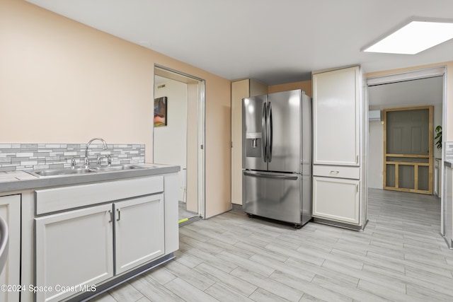 kitchen featuring sink, stainless steel refrigerator with ice dispenser, backsplash, white cabinets, and light wood-type flooring